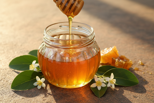 Golden Sidr honey dripping from a wooden honey dipper into a glass jar with sidr tree leaves and flowers on a stone surface