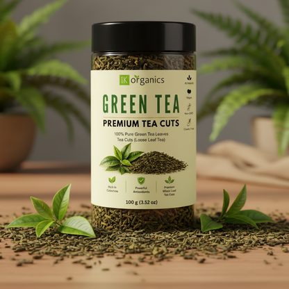 A 100g jar of IK Organics Green Tea Premium Tea Cuts loose leaf tea, featuring a cream-colored label and a black lid, set against a soft beige fabric background.